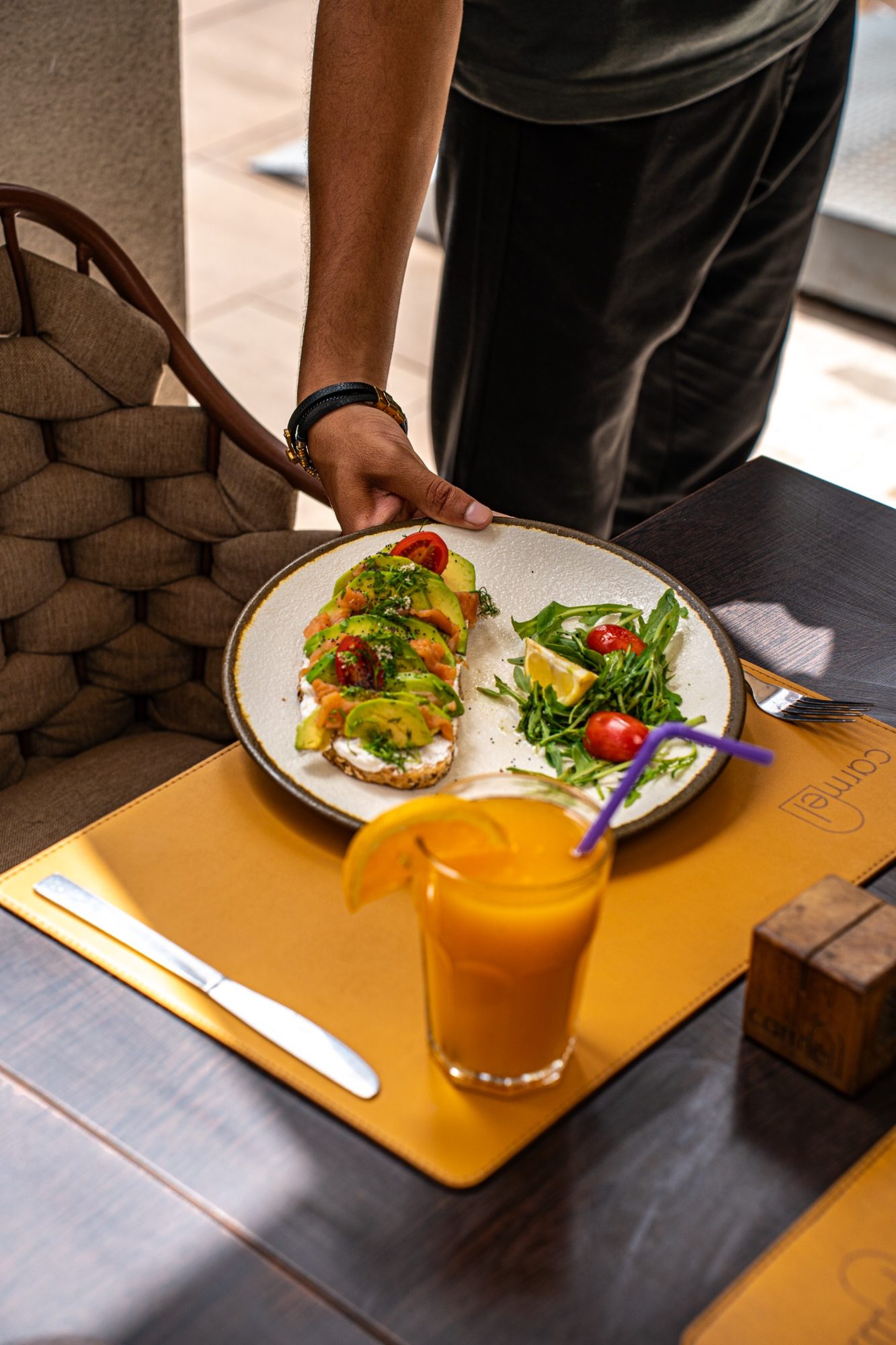 Un membre de l'équipe Carmel servant un toast à l'avocat et un jus d'orange frais