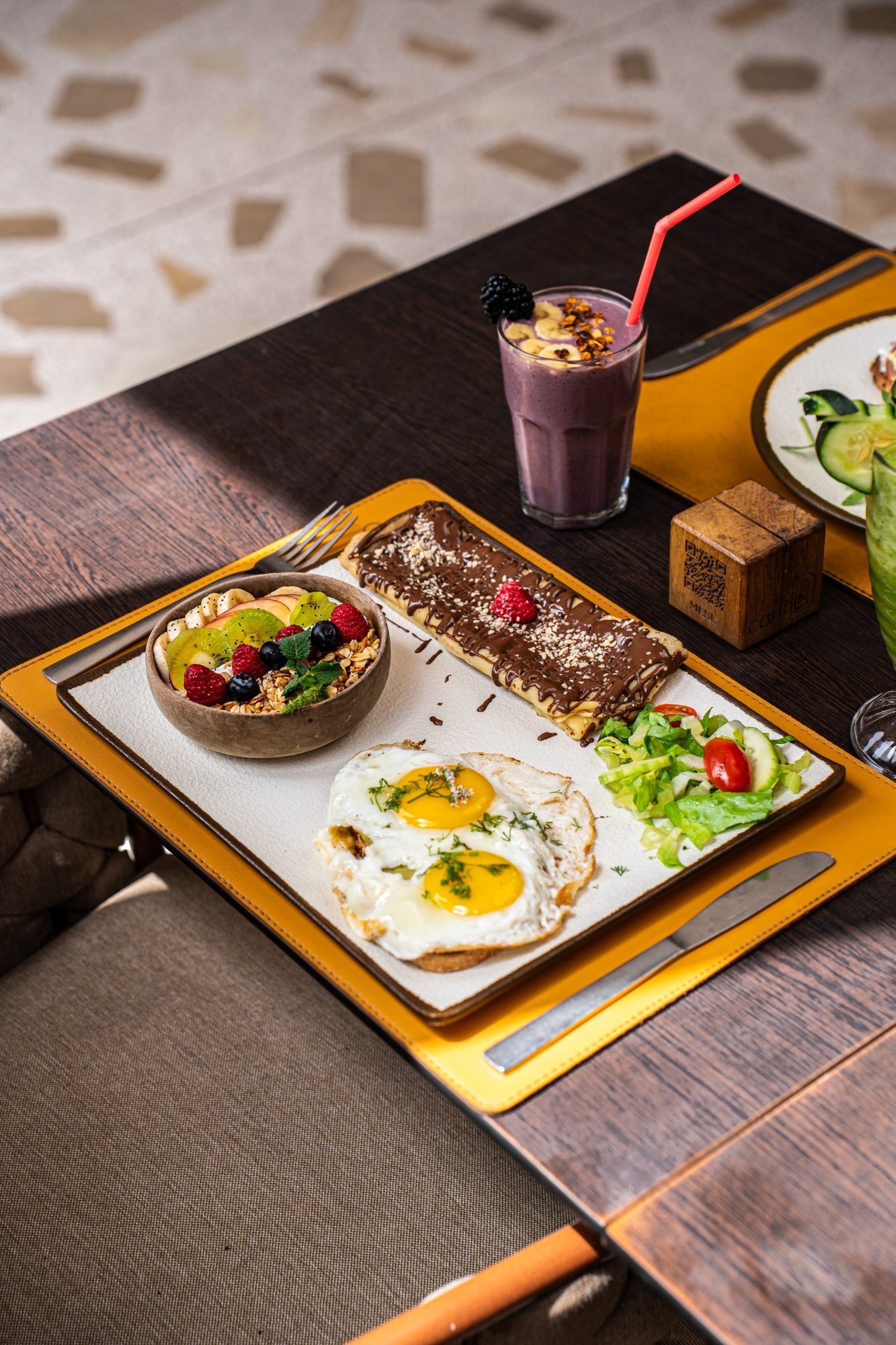 Plateau de brunch avec œufs au plat, bol de granola et smoothie aux baies